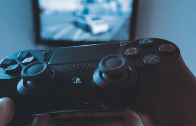 Someone holds a Playstation controller in front of an out-of-focus television