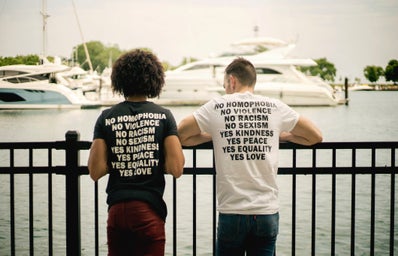 Two people wearing shirts that have text about activism look out over a harbor