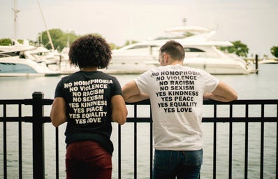 Two people wearing shirts that have text about activism look out over a harbor