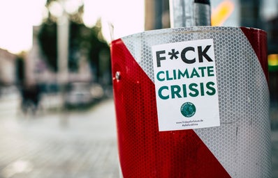 A white and red trash can/bin has a sticker on it that says "F*CK Climate Crisis"