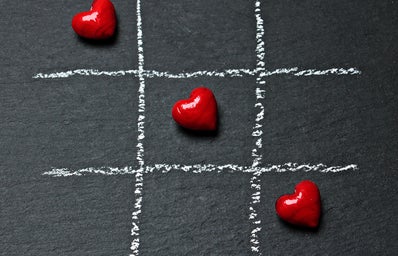 Three red candy hearts stand out against a grey background in a game of tic-tac-toe