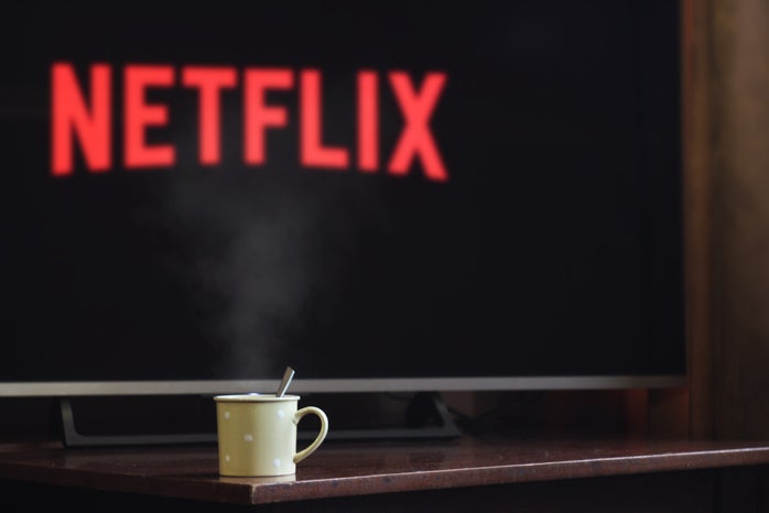 A fuzzy screen in the back ground might say "netflix" but the image's selective focus is on a mug of some sort.