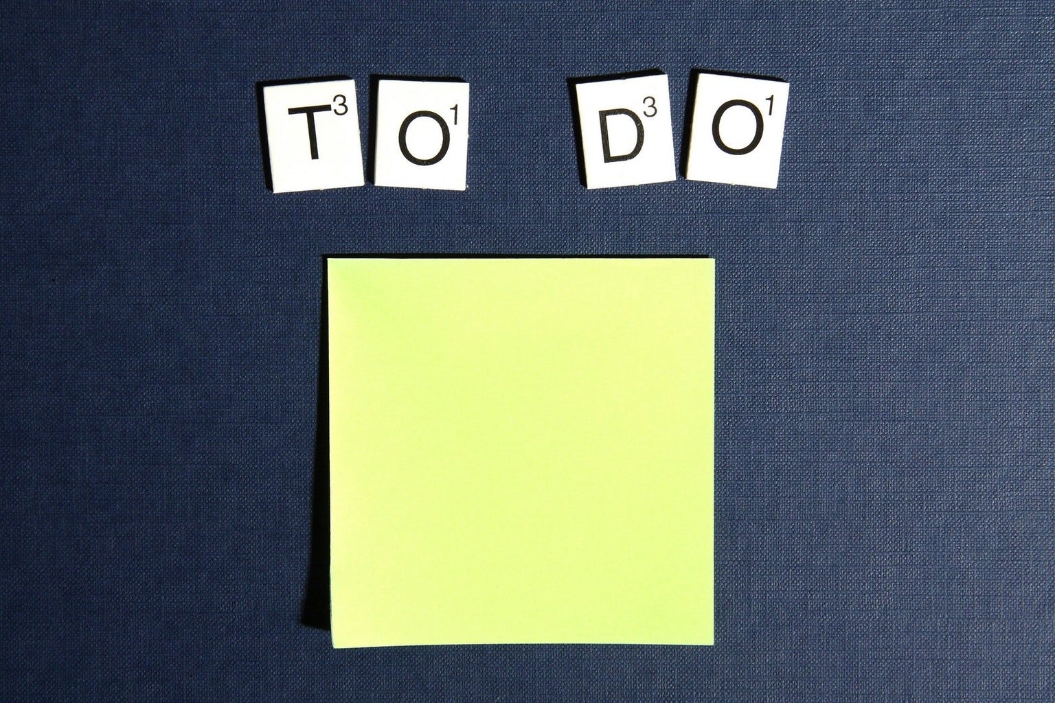 Scrabble tiles spell out \"To Do\" on a blue background above a yellow sticky note