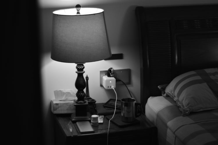 black and white nightstand with lamp, tissues, mug, and charger