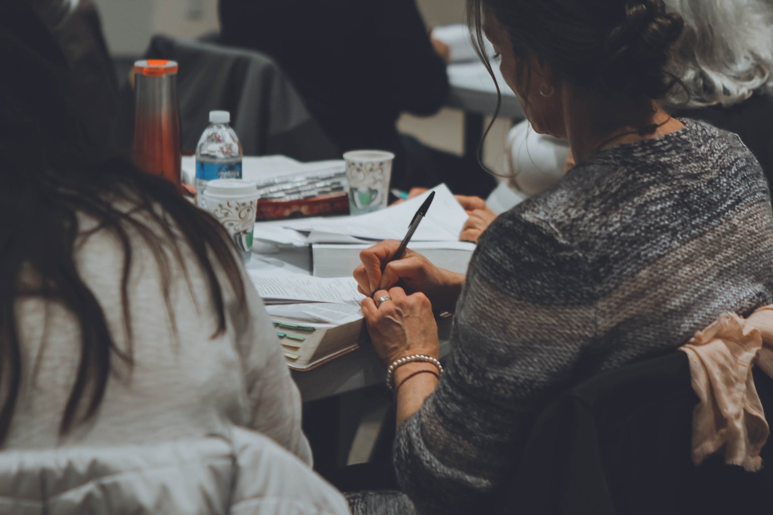 woman in a gray sweater taking notes on white paper