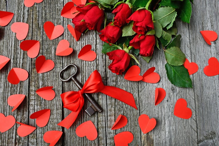 rose bouquet, red paper hearts, and key wrapped in ribbon scattered on a gray surface