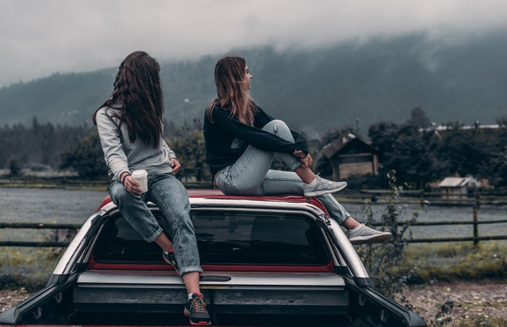 Two girls sitting on sitting on the hood of a car