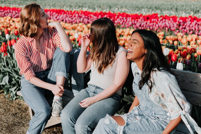 Three women talking and laughing on the wooden bench next to the tulip flower field