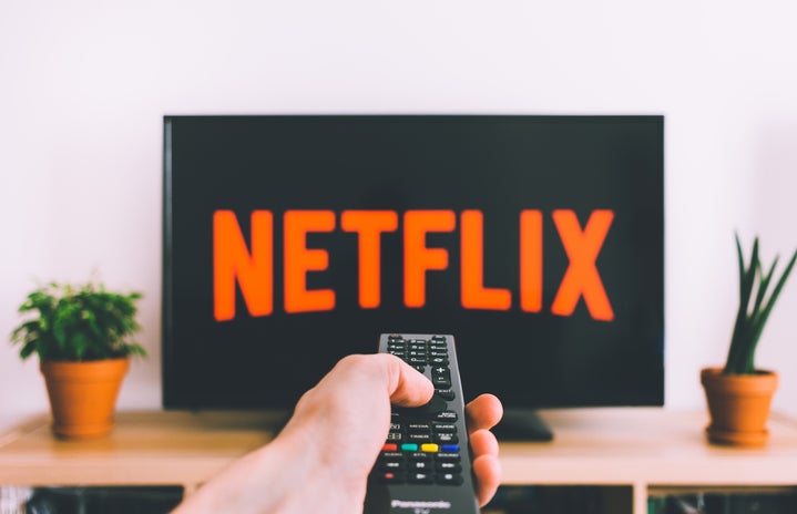 Netflix symbol on TV with a hand holding a remote