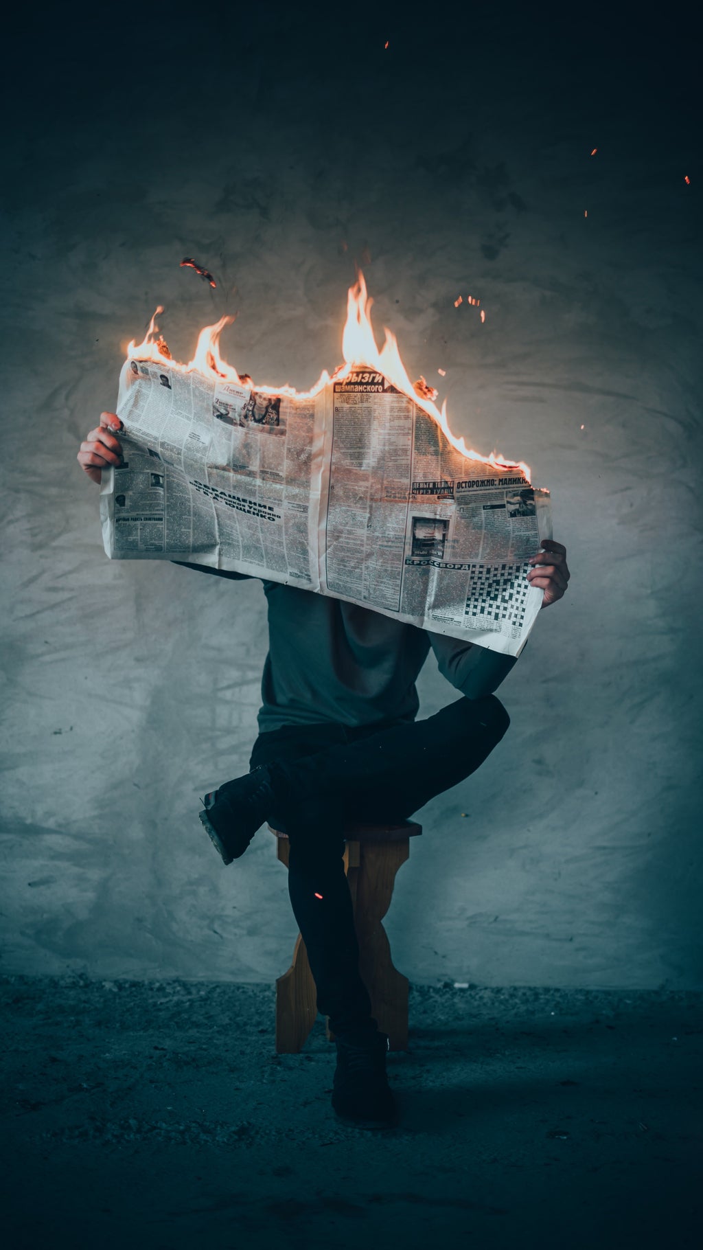 Man sitting with leg crossed reading a newspaper that is on fire.