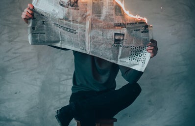 Man sitting with leg crossed reading a newspaper that is on fire.