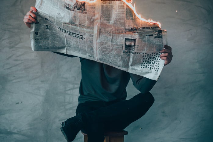 Man sitting with leg crossed reading a newspaper that is on fire.