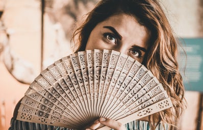 Woman holding a fan over her face