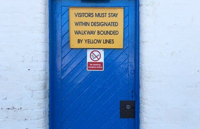 Blue door with a yellow sign asking visitors to stay outside and a \'no smoking\' sign