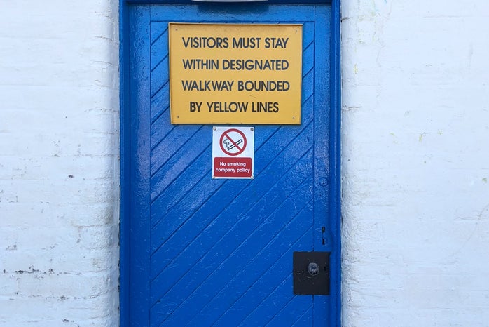 Blue door with a yellow sign asking visitors to stay outside and a \'no smoking\' sign