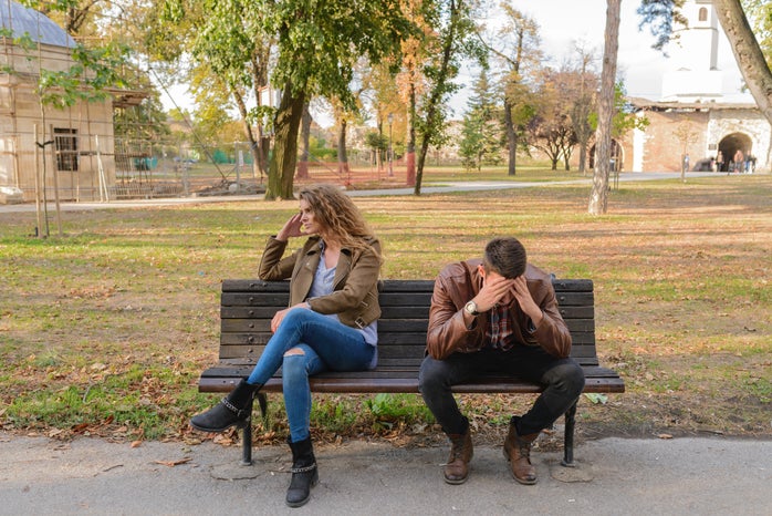 a man and a woman sit on a park bench looking frustrated