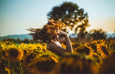 woman standing in sunflower field flipping her hair
