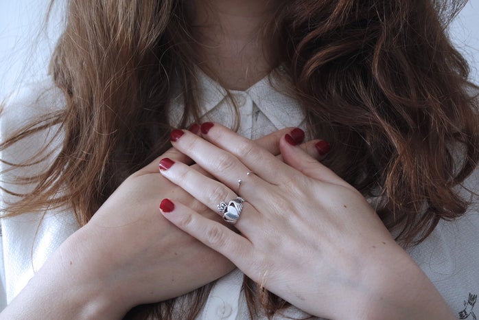 woman wearing silver-colored Claddagh ring with crossed hands and red nail polish on