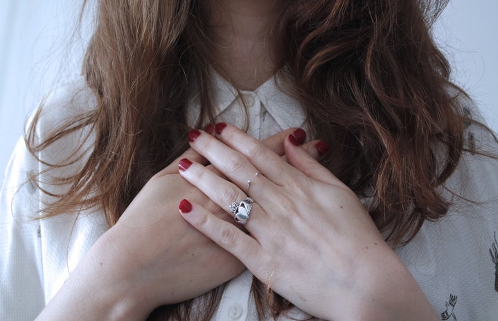woman wearing silver-colored Claddagh ring with crossed hands and red nail polish on