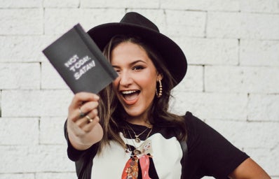 Woman in a black hat holding a book that says \"not today Satan\"