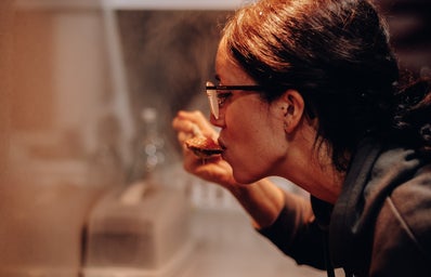 a woman leans over a pan of food, taste-testing it