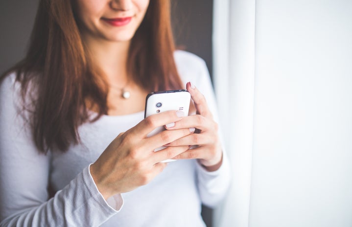 woman in a white shirt holding her cell phone in front of her