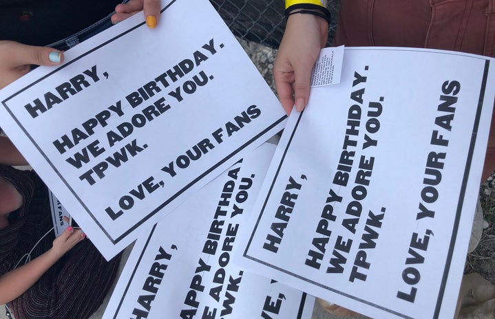 Women holding signs that say \"Happy Birthday Harry\" at a Harry Styles concert