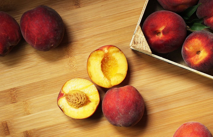 A halved peach sits on a table near other whole peaches.