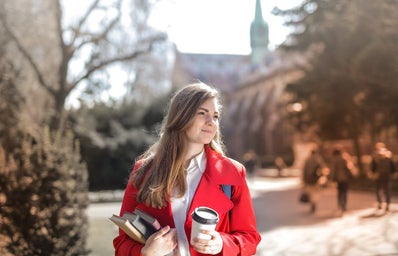 woman in red coat business casual holding books and a coffee