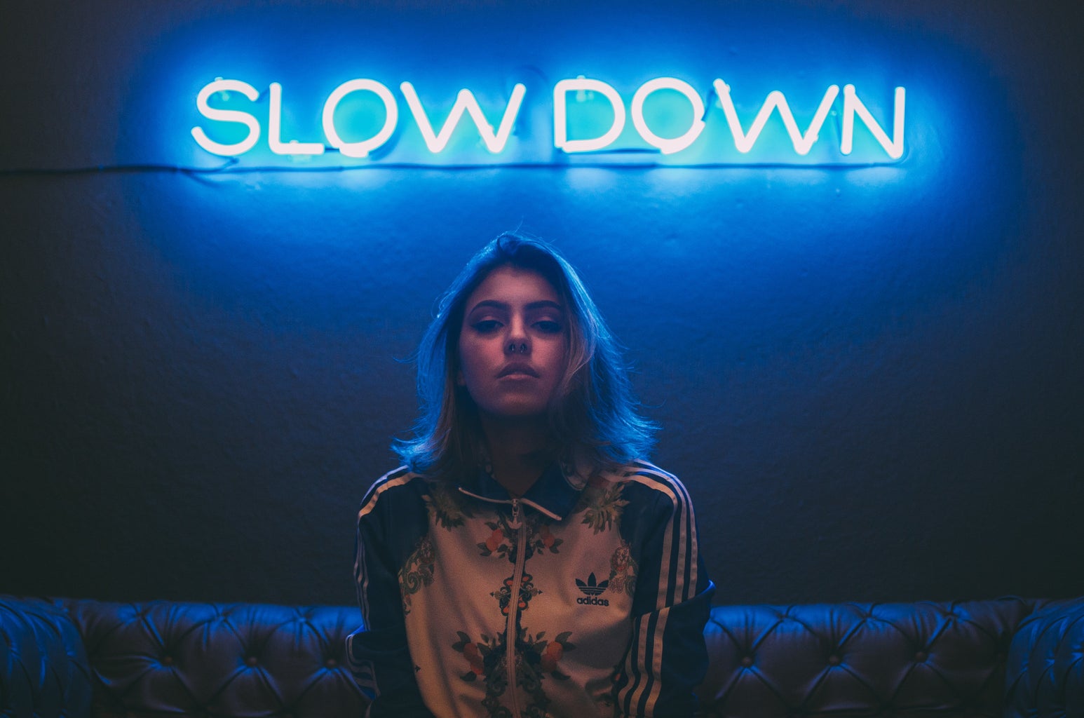 woman sitting on a brown sofa in front of a neon sign that says 