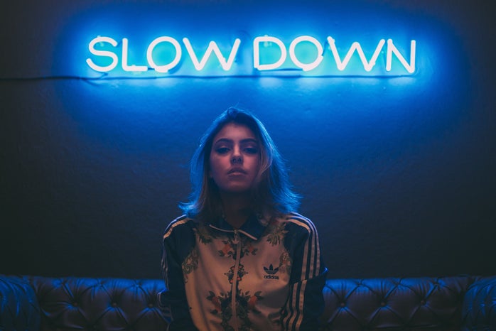 woman sitting on a brown sofa in front of a neon sign that says "slow down"