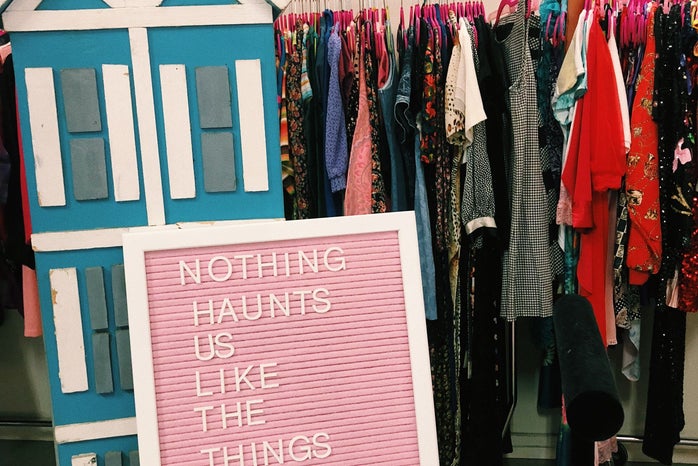 A pink board that says “Nothing Haunts us like the things we didn’t buy” with clothes in the background