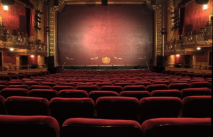 An ornate theatre with red chairs and stage curtain.