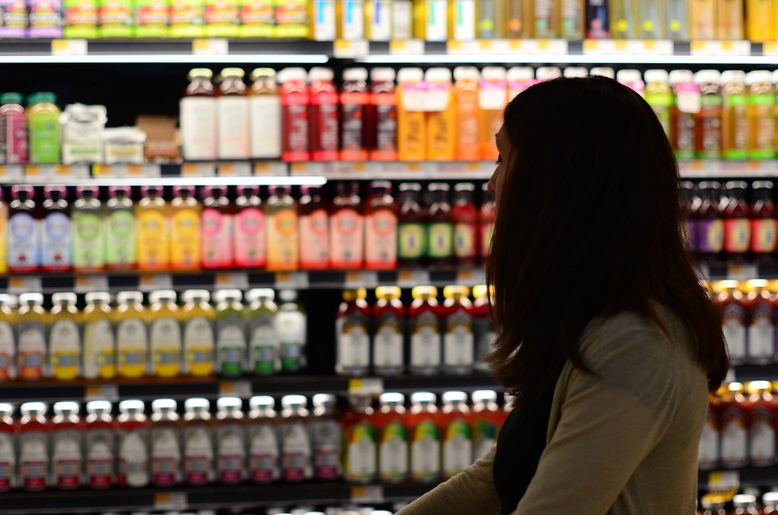a woman stands in front of the health juice/kombucha shelves at a grocery store
