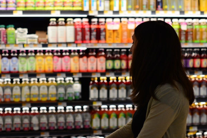 a woman stands in front of the health juice/kombucha shelves at a grocery store