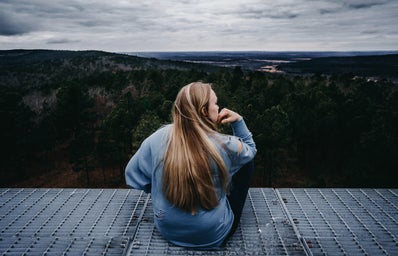 a woman sits on the edge of a deck overlooking the forest