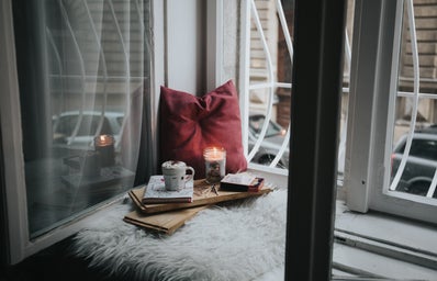 A cozy window nook with a candle, hot chocolate and a book.