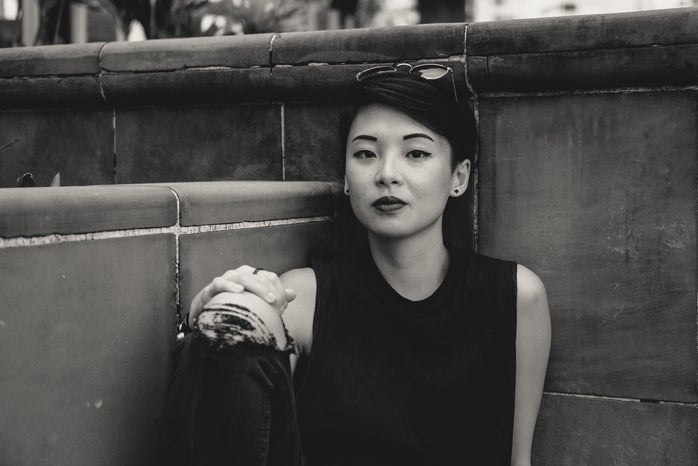 grayscale photo of Asian woman sitting at the corner of wall