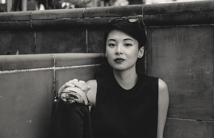 grayscale photo of Asian woman sitting at the corner of wall