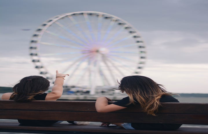 Girls on bench in front of ferris wheel