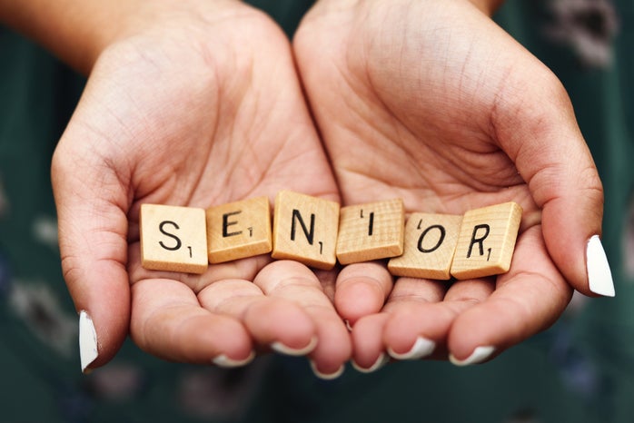 A girl with white nail polish holding scrabble letters spelling the word SENIOR