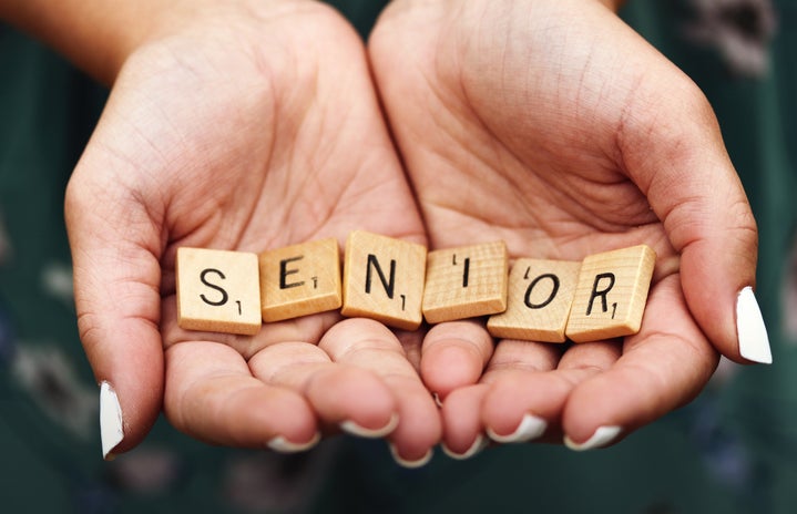 A girl with white nail polish holding scrabble letters spelling the word SENIOR