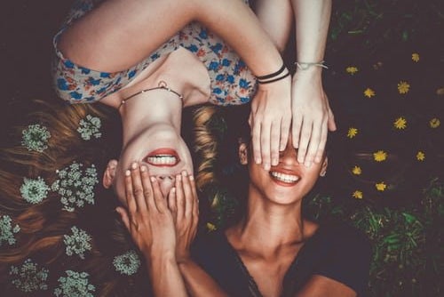 Two girls laying in the grass with flowers covering their faces