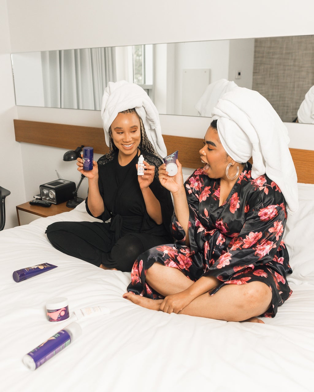 friends sitting on bed holding beauty products