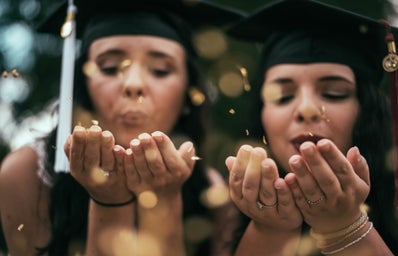 two women blowing glitters from palms during daytime