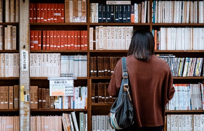 Woman Wearing Brown Shirt Carrying Black Leather Bag on Front of Library Books