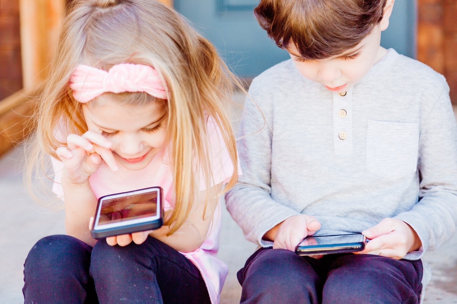 Two children sitting on the steps looking at their phones
