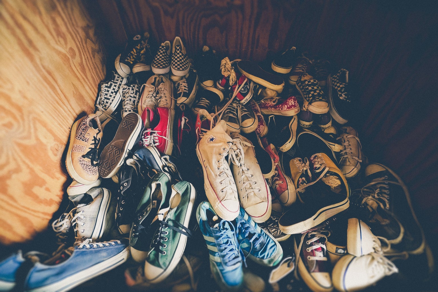 a pile of sneakers, converse and vans sit at the bottom of a closet.