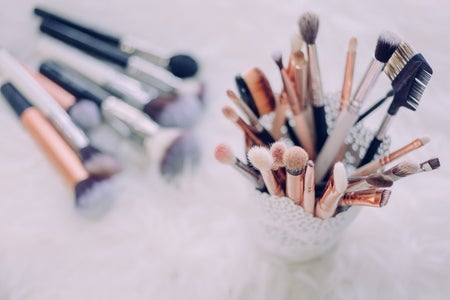 a cup of makeup brushes is in focus on the right, and a small handful of brushes lays out of focus on the table to the left