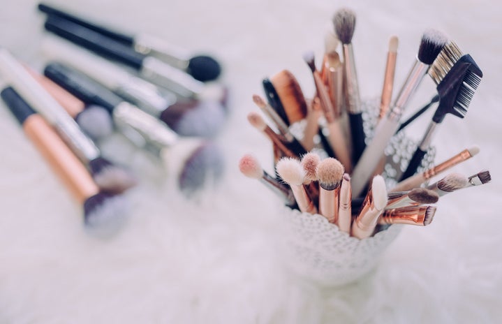 a cup of makeup brushes is in focus on the right, and a small handful of brushes lays out of focus on the table to the left